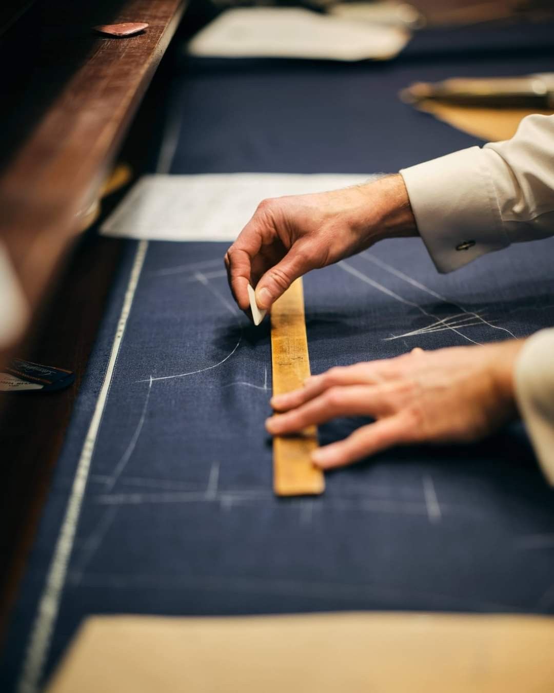 A tailor marking navy cloth with chalk and a wooden ruler